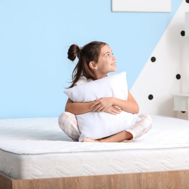 Morning of little girl sitting on bed with comfortable mattress
