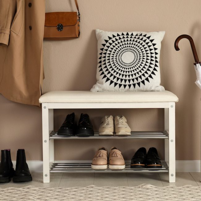 Stylish storage bench with different pairs of shoes near beige wall in hall